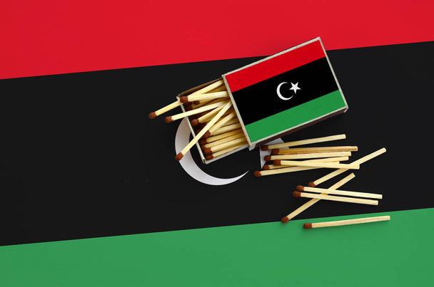 Die libysche Flagge wird auf einer offenen Streichholzschachtel gezeigt, aus der mehrere Streichhölzer fallen und auf einer großen Fahne liegen.. - Foto, Bild
