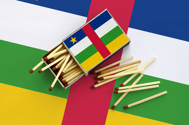Bandera de la República Centroafricana se muestra en una caja de fósforos abierta, de la que caen varios partidos y se encuentra en una gran bandera
. - Foto, Imagen