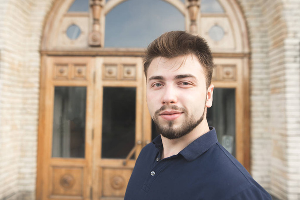 Portrait of beautiful man with beard on background of university door. Close-up portrait of a student on the background of the university building. - Fotó, kép