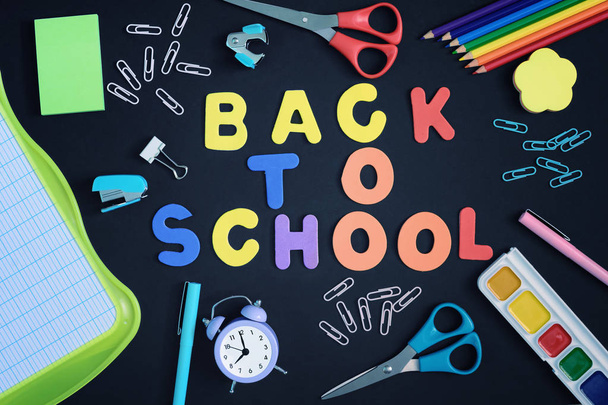 Chaotically spread out stationery on a black background. In the center there is an inscription made in colored letters. Back to school. Bright photo from the top. - Foto, afbeelding