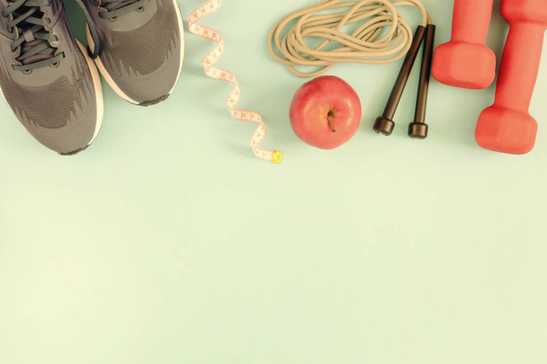 On a pale blue surface lie red dumbbells, sneakers, a skipping rope and an apple. Bottom of the place for the inscription, mock up. Fitness background. - Photo, Image