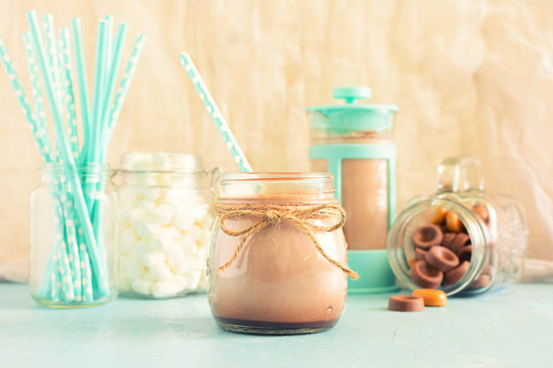 Forró kakaót van öntött levegőbe korsó. A háttér, kávé pot, marshmallows és csokoládé édességek. A háttérben a bokeh. - Fotó, kép