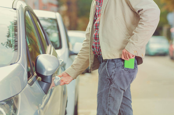 człowiek, biorąc pod uwagę smartfona w kieszeni podczas otwierania drzwi samochodu na ulicy - Zdjęcie, obraz