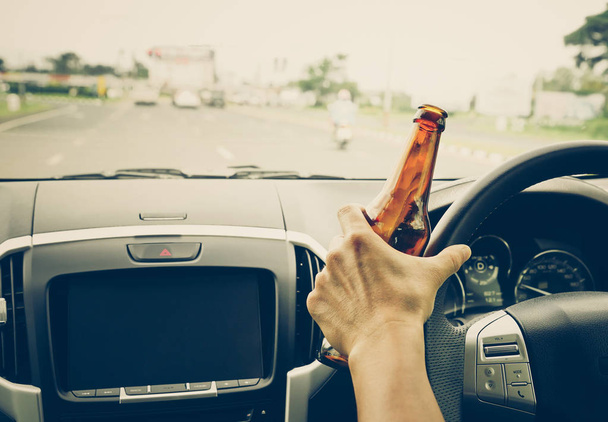 Un conductor sosteniendo una botella alcohólica mientras conduce / concepto de conducción ebria
 - Foto, Imagen