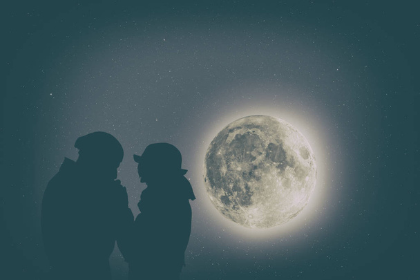 романтичный мужчина целует подругу руки, стоя на фоне ночного неба с большой луной и звездами
  - Фото, изображение