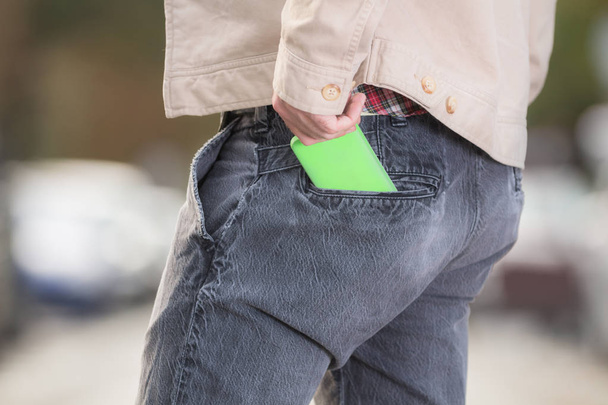 homem tirando smartphone verde de bolso de calça na rua borrada
  - Foto, Imagem