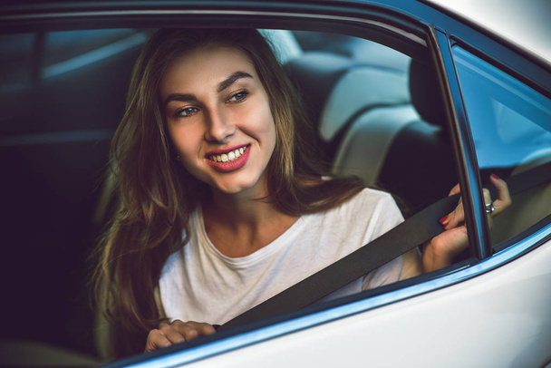 Mulher bonita com telefone sorrindo enquanto sentado no banco de trás no carro
. - Foto, Imagem