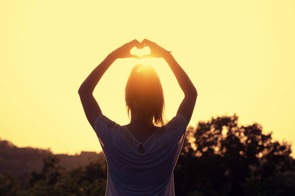vista posteriore della donna con le mani alzate che mostrano il segno del cuore al tramonto sullo sfondo del cielo
 - Foto, immagini