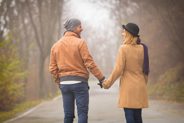 sweet couple holding hands and walking on road in autumn park - Photo, Image