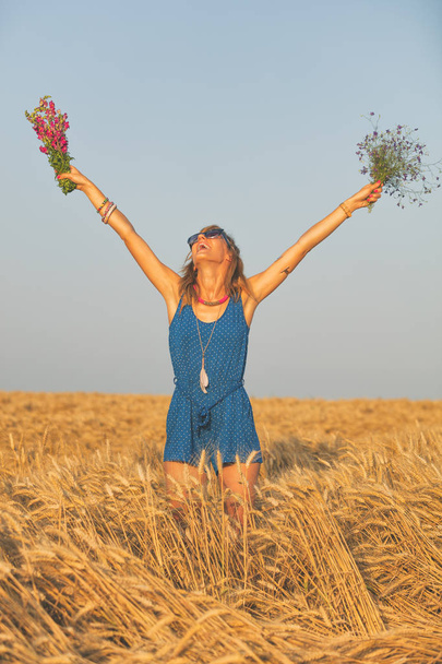 woman raised hands with two wildflower bouquets in barley meadow  - Photo, Image