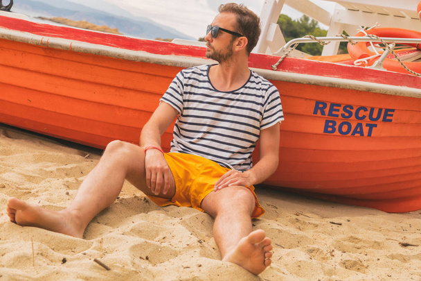 Badmeester poseren met zijn boot op het strand - Foto, afbeelding
