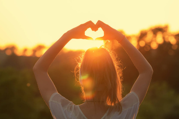 Hátulnézet nő felemelt kézzel mutatja a szív jel napsütötte homályos ég előzmények - Fotó, kép