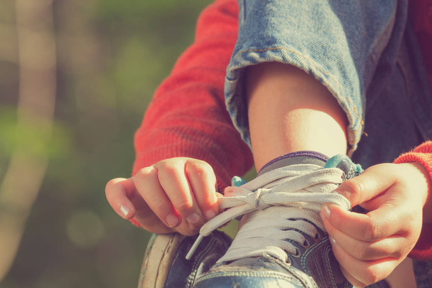 niña atando cordones de zapatos mientras está sentada sobre un fondo natural borroso, de cerca
  - Foto, imagen