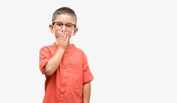 Criança de cabelos escuros usando óculos cobrir a boca com a mão chocada com vergonha de erro, expressão de medo, assustado em silêncio, conceito secreto
 - Foto, Imagem