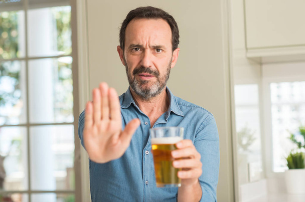 Keski-ikäinen mies juo olutta avoimella kädellä tekemällä stop-merkin vakavalla ja itsevarmalla ilmeellä, puolustus ele
 - Valokuva, kuva