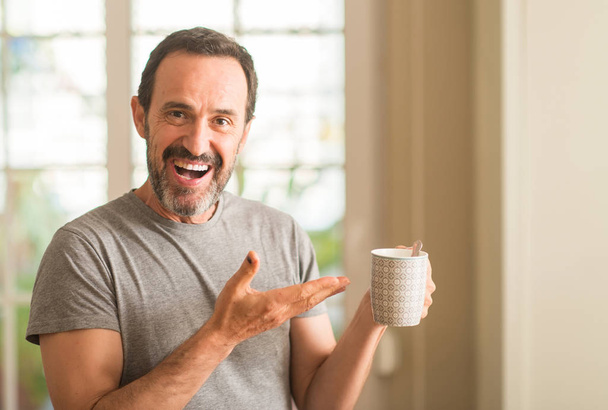 Homem de meia idade bebendo café em uma xícara muito feliz apontando com a mão e o dedo
 - Foto, Imagem