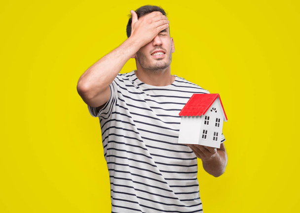 Handsome real estate agent holding a house stressed with hand on head, shocked with shame and surprise face, angry and frustrated. Fear and upset for mistake. - Фото, изображение
