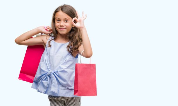 Brunetka hispánský dívka drží nákupní tašky dělá ok cedulka s prsty, vynikající symbol - Fotografie, Obrázek