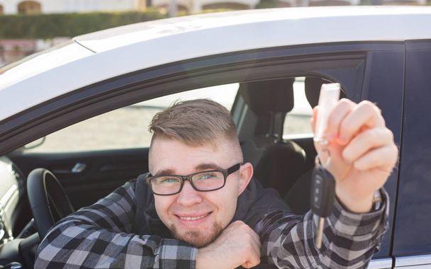 Счастливый молодой человек сидит в машине с ключами от машины
 - Фото, изображение
