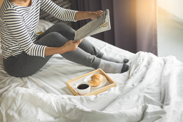 Woman reading book or newspaper and drinking coffee breakfast on bed during the morning. - Photo, image