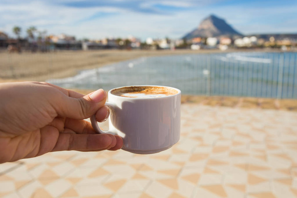 Tasse Kaffee in der Hand vor dem Hintergrund eines schönen Strandes. - Foto, Bild