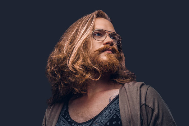 Close-up portrait of a redhead hipster male with long luxuriant hair and full beard dressed in casual clothes standing in a studio, looking away. Isolated on a dark background. - Foto, Imagem