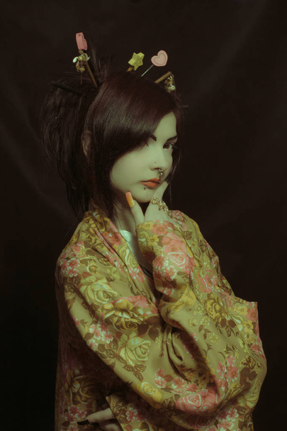 Pretty geisha in kimono posing over dark background - Photo, image