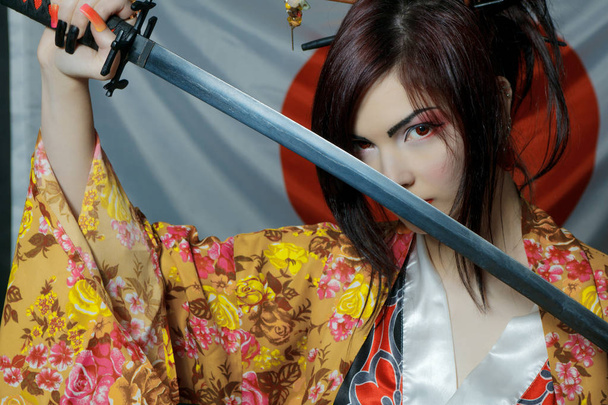 Cute girl in kimono posing over japanese flag with katana - 写真・画像