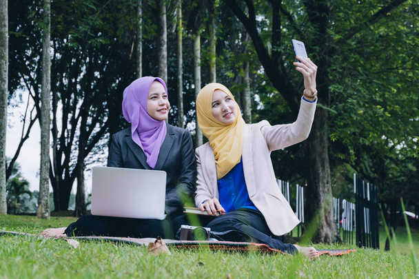 fröhliche professionelle Muslima, die Spaß hat, Zeit miteinander verbringt und Selfies im Stadtpark macht - Foto, Bild