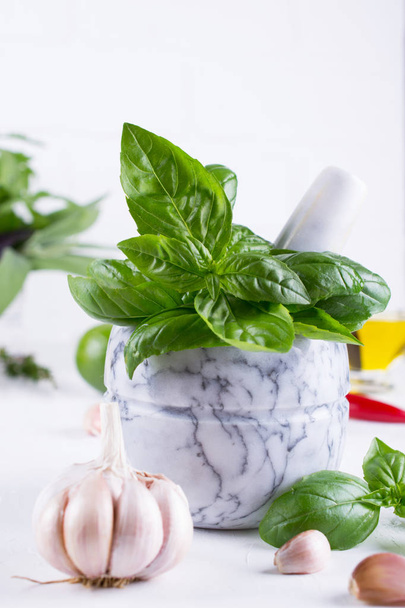 Fresh garden basil herbs in mortar and olive oil, garlic , red hot chili peppers, lemon on the white background. - Zdjęcie, obraz