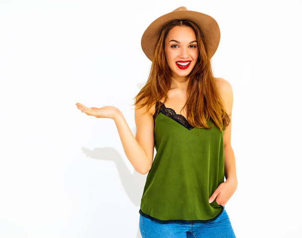 Young stylish girl model in casual summer green clothes and brown hat with red lips holding something on her hand, isolated  - Fotoğraf, Görsel