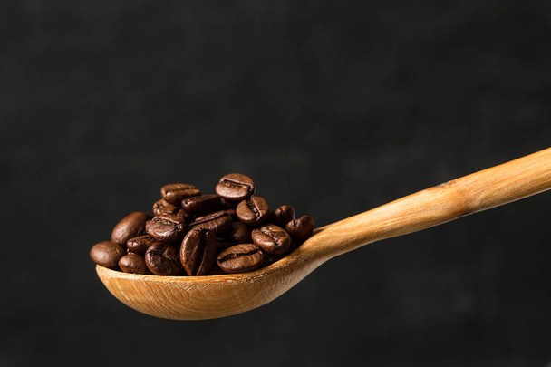 Roasted coffee beans in a wooden spoon on gray background.  Food ingredients,  space for text - Фото, зображення