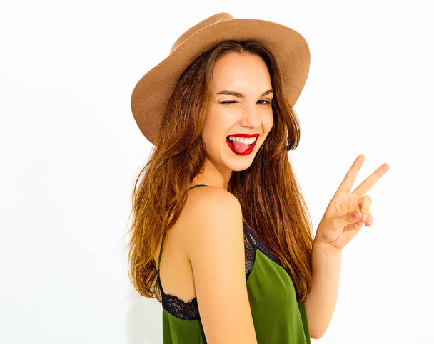 Young stylish girl model in casual summer green clothes and brown hat with red lips. Winking and showing her tongue - Valokuva, kuva