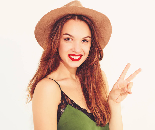 Young stylish girl model in casual summer green clothes and brown hat with red lips, showing peace sign - Foto, Imagem
