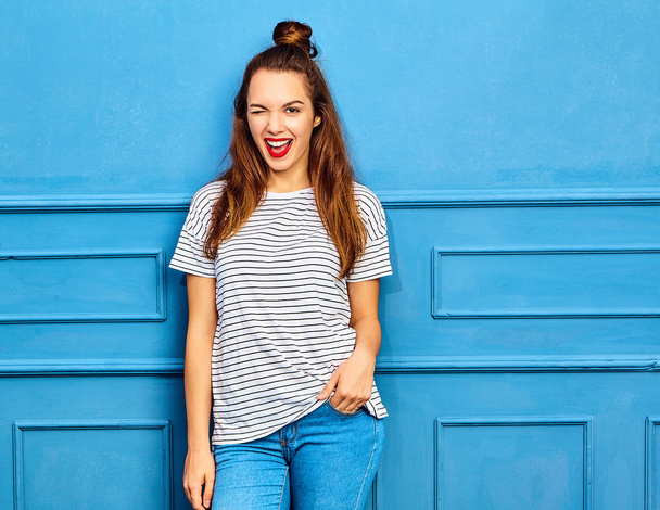Młoda dziewczyna stylowy model w codzienne letnie ubrania z czerwonymi ustami, pozowanie w pobliżu niebieską ścianą. Mrugając - Zdjęcie, obraz