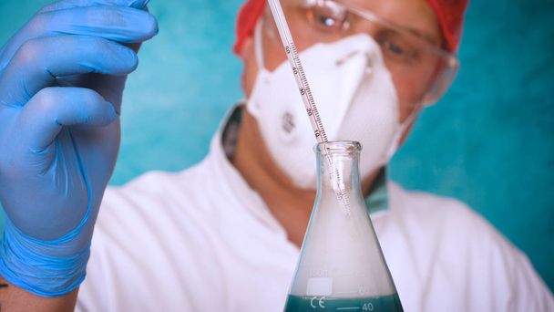 Алхимик, биолог, берет ДНК различных веществ, в респираторе, в защитной фуражке, в очках, в белом медицинском платье, фляжке, зеленом фоне, научном столе
. - Фото, изображение