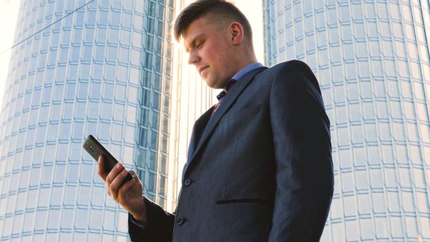 Young handsome businessman talking on phone, in costume, skyscraper - Photo, Image