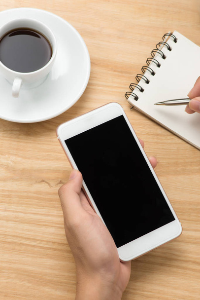 Man hand holding smart phone and pen with white blank empty screen on white desk table.Business concept. - 写真・画像