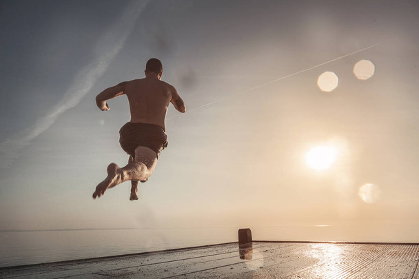 A young man is jumping from the pier into the water at sea in the summer. - Foto, imagen