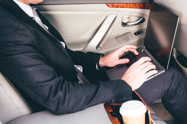 Beau homme d'affaires travaillant sur ordinateur portable assis sur le siège arrière d'une voiture
 - Photo, image