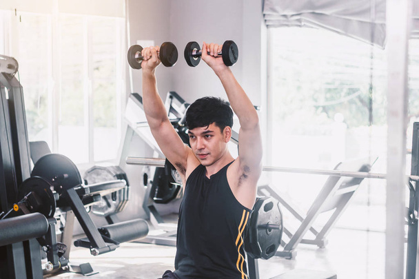 Spor salonunda oturan dumbbell ile ağırlık egzersizleri yapıyor fitness adam - Fotoğraf, Görsel