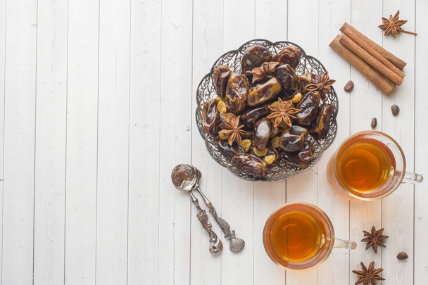 Oriental sweets, dried fruit dates and raisins, cinnamon and star anise in a plate. Turkish tea in glasses on a wooden background - Фото, изображение