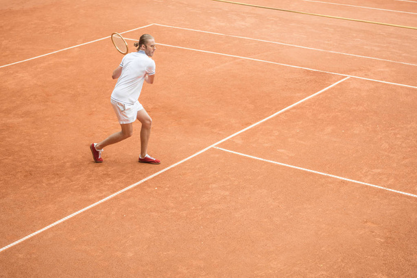 altmodische männliche Tennisspielerin mit Schläger auf braunem Tennisplatz - Foto, Bild