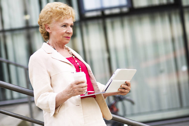 Блондинка деловая женщина. Пожилая деловая женщина с кофе и планшетом, на открытом воздухе
. - Фото, изображение