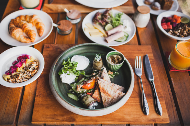 Восточный завтрак с яичницей, помидорами, кускусом, баклажанами и острым соусом в керамической тарелке на деревянном подставке
 - Фото, изображение