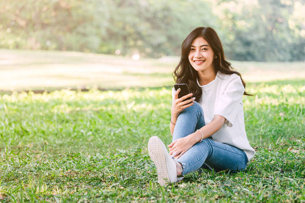 Γυναίκα να χαλαρώσετε και να χρησιμοποιείτε το smartphone κάθεται στο γρασίδι στο πάρκο - Φωτογραφία, εικόνα