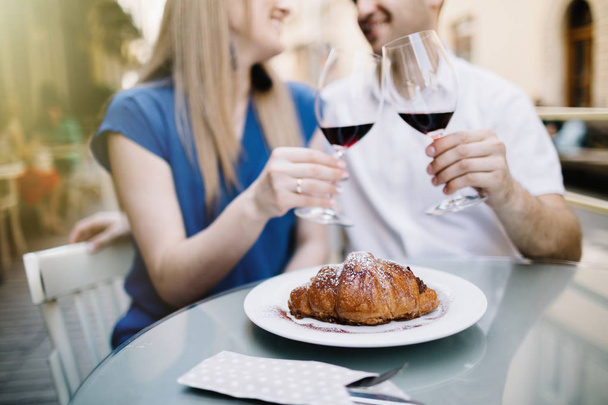 Cheers. Young loving couple sitting close to each other smiling and  toasting with two red wine glasses. - Φωτογραφία, εικόνα