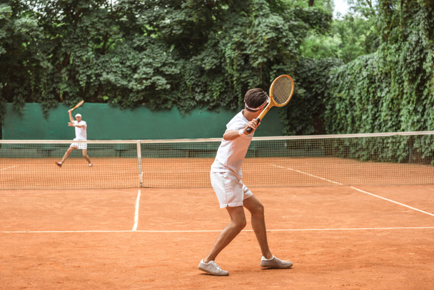 sportsmen in white sportswear playing tennis with wooden rackets on court - Photo, Image