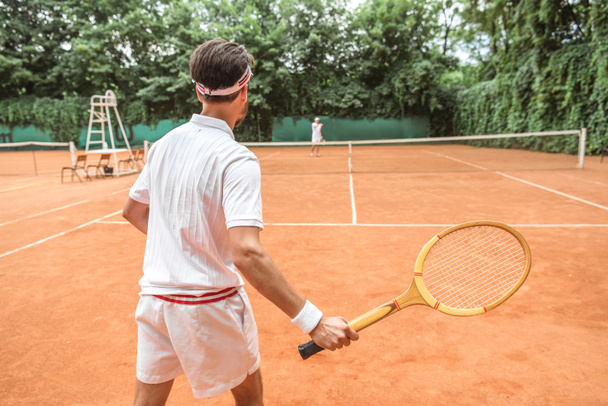 вид сзади спортсмена, играющего в теннис с деревянной ракеткой на теннисном корте
 - Фото, изображение