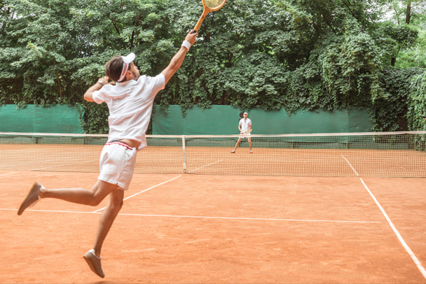 спортсмен прыгает во время игры в теннис с другом на корте
 - Фото, изображение